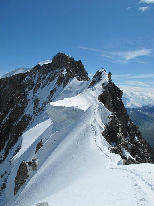 A corniced snow ridge running out towards a rocky summit